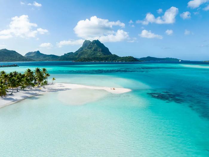Aerial view of a white sand motu and turquoise lagoon in Bora Bora with Mount Otemanu